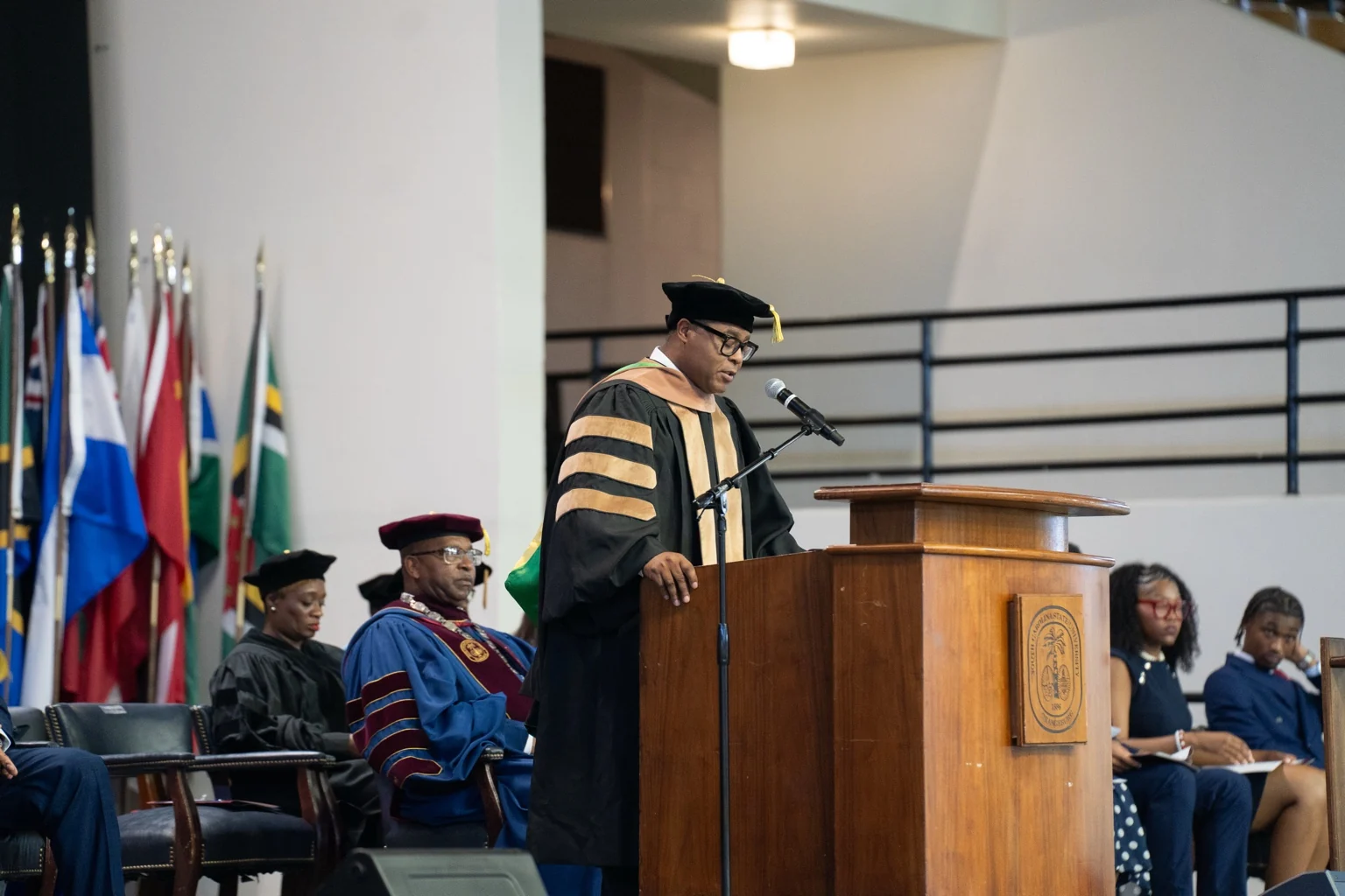 Speaker in academic regalia delivering remarks at a university ceremony